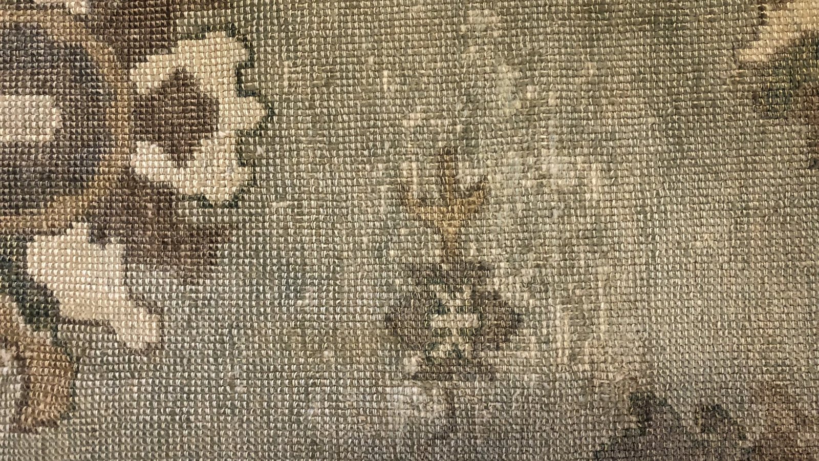 The reverse of a wool rug under inspection lighting, where the foundation shows what the pile is hiding